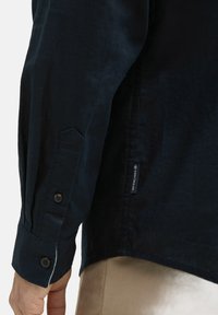 Marineblauwe overhemd met knopen, gekenmerkt door een gladde textuur, schuine manchetten en een logo-label aan de zijnaad. Het materiaal lijkt lichtgewicht en casual te zijn.