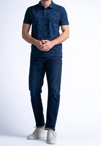 Marinblå pikétröja med subtilt blommönster, kortärmad och med krage. Bärs med mörkblå jeans och ljusa sneakers.