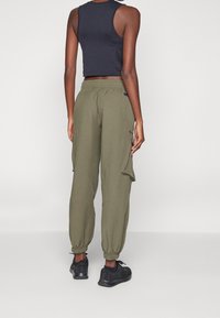 Olivgröna cargobyxor med elastiska muddar, sidfickor och avslappnad passform, kombinerade med ett svart, kort linne och svarta sneakers.