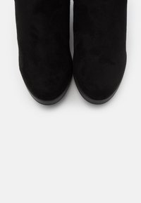 Bottines en daim noir à texture lisse et bout arrondi, dotées d'une semelle plate noire et d'un design minimaliste.