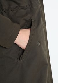 Chaqueta verde oliva con un bolsillo lateral con cierre de botón, costuras reforzadas y un acabado suave y texturizado.