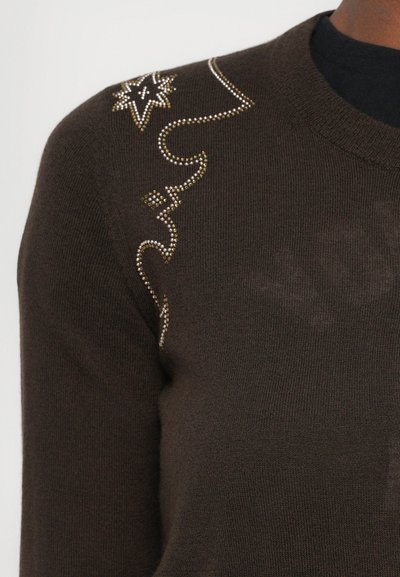 Bruine trui met een ronde hals en ribbelstructuur, voorzien van decoratieve strassteentjes in een spiraalpatroon op de schouder.