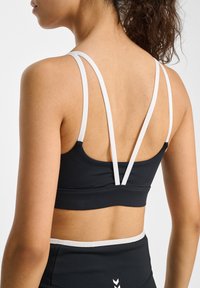 Svart sport-bh med vita detaljer. Har tunna, justerbara axelband och en rundad ryggdesign. Slät tygtextur och minimalistisk stil.