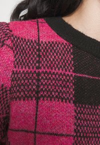 Rosa-schwarzer Strickpullover mit kariertem Muster in verschiedenen Schattierungen, schwarzem Rippkragen und weicher Textur.