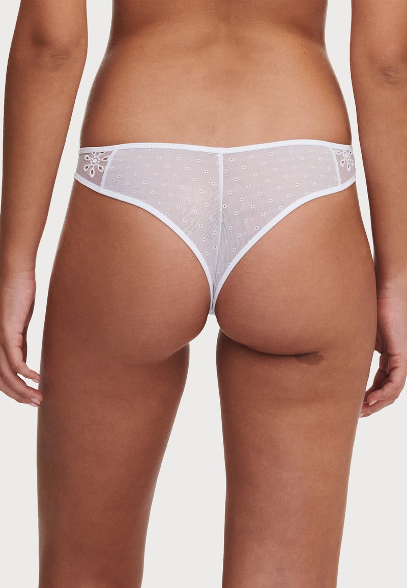 Tanga de lencería blanca con tela de malla de lunares, con detalles de encaje. Diseño de corte bajo que acentúa un patrón floral en los lados.