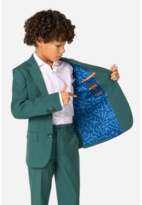 Soprabito verde con una vestibilità su misura, tessuto testurizzato, giacca monopetto e fodera blu a motivo. Include una camicia bianca e dettagli con bottoni.