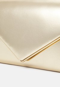 Pochette ton or en matériau métallique lisse, avec un rabat diagonal au design triangulaire élégant et une subtile brillance.