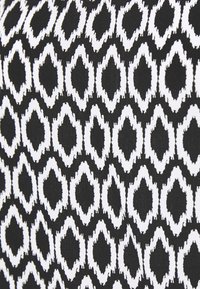 Tissu noir avec un motif ikat blanc répété, présentant des formes allongées en losange et des bords effilochés, créant une apparence texturée.