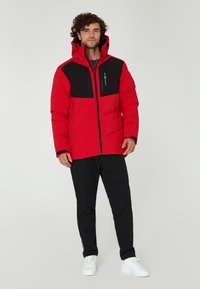 Röd isolerad jacka med svarta detaljer, dubbla dragkedjefickor och huva. Bärs med svarta byxor och vita sneakers.