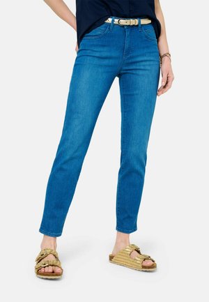 Schlanke blaue Denim-Jeans mit hoher Taille, Fronttaschen und einem goldenen Gürtel. Getragen mit goldenen, geflochtenen Sandalen mit einer klobigen Sohle.