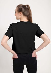 Czarny t-shirt z krótkim rękawem, wykonany z bawełny, z klasycznym okrągłym dekoltem i luźnym krojem, przedstawiony z tyłu.