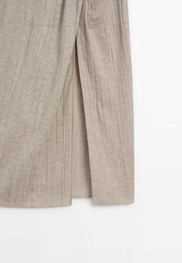 Tissu tricoté beige côtelé avec une fente centrale, montrant la texture et des lignes verticales sur la partie inférieure d’un vêtement.