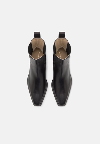 Botas de tobillo de cuero negro con puntera puntiaguda, paneles laterales elásticos y tiradores en el talón, con una textura suave y brillante.