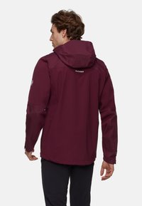 Giacca impermeabile bordeaux con cappuccio, dettagli in gomma e tasche con zip; presenta un materiale testurizzato e un logo sul retro.