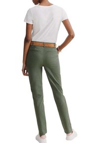 Pantalons verts avec une coupe ajustée, dotés de poches arrière et d'une ceinture marron. Associés à un haut blanc à manches courtes et des baskets blanches.