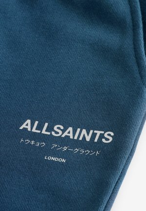 Sötétkék textil bordázott textúrával. Jól látható fehér "ALLSAINTS" felirat, alatta japán nyelvű szöveggel, legalul pedig "LONDON".