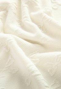Biała, teksturowana tkanina z delikatnym wzorem tkanym, o miękkim, pomarszczonym wyglądzie. Lekka i uniwersalna, przeznaczona do różnych zastosowań.