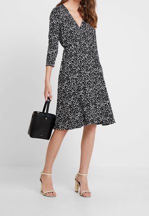 Black and white patterned dress with a V-neck, 3/4 sleeves, and a flared hem, paired with black handbag and beige high-heeled sandals.