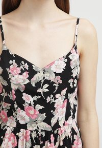 Blommig klänning med svart bakgrund och rosa och vita blommor, v-ringning, tunna band och en plisserad kjol. Slät tygkvalitet.