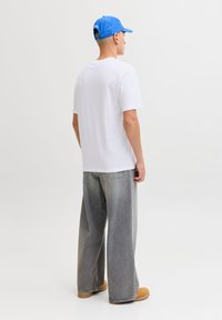 Άσπρο μπλουζάκι, φαρδιά εφαρμογή, γκρι τζιν με φαρδιά πόδια, παπούτσια ταμπά, μπλε καπέλο. Απλό, casual σύνολο με ελάχιστες λεπτομέρειες.