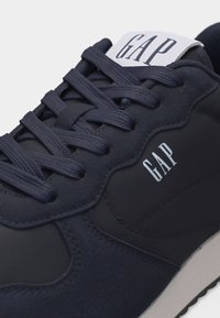 Gros plan sur une basket bleu marine avec des lacets bleu marine, une semelle blanche et le logo blanc "GAP" sur la languette et le côté.