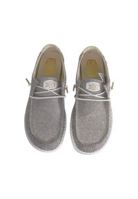 Silver glitter slip-on shoes with a rounded toe, white accents, and a logo patch on the tongue. Textured surface with a flat sole.
