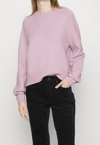 Pull tricoté violet clair avec ourlet et poignets côtelés, présentant une coupe décontractée. Associé à un pantalon noir taille haute.