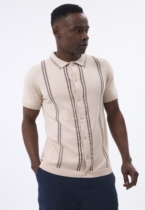 La camiseta polo de manga corta beige presenta rayas verticales marrones, un cierre de botones y un collar clásico. Está hecha de una suave tela texturizada.