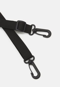 Correia de nylon preta com dois ganchos de pressão, fivela ajustável e superfície texturizada. Os ganchos são moldados para uma fixação segura.