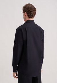 Czarna koszula z długim rękawem, klasycznym kołnierzem i mankietami na guziki, wykonana z gładkiej tkaniny, o prostym kroju i zaokrąglonym dolnym brzegu.