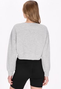 Grå kort sweatshirt med långa ärmar och ribbade muddar, i kombination med svarta höga shorts. Mjuk textur, avslappnad design.