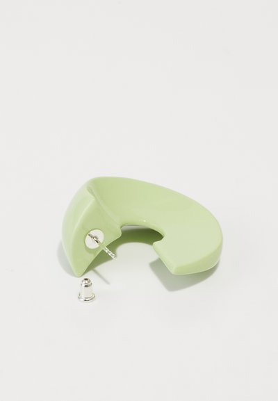 Accesoriu ceramic verde, cu o formă curbată, dotat cu un ac din metal. Textură netedă, cu finisaj lucios și un mic sistem de prindere metalic.