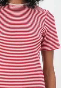 Tricou cu dungi roșii și albe, realizat dintr-un material ribbed, cu mâneci scurte și guler rotund, textura fiind vizibilă datorită modelului materialului.