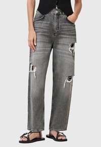 Versleten grijze denim jeans met een wijd beenpas, voorzien van rafelige scheuren en een vervaagde afwerking. Gepaarde met zwarte platte sandalen.