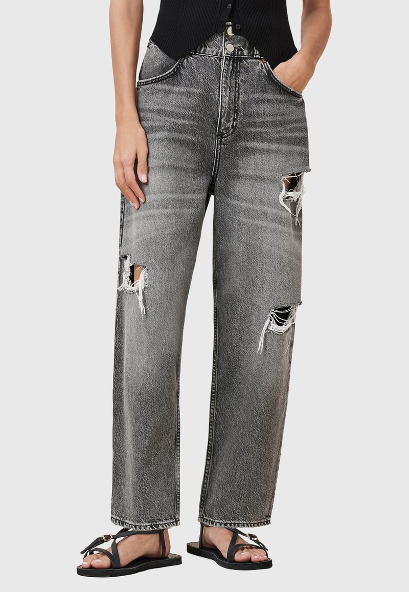 Versleten grijze denim jeans met een wijd beenpas, voorzien van rafelige scheuren en een vervaagde afwerking. Gepaarde met zwarte platte sandalen.