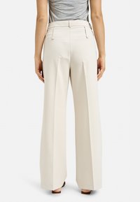 Wide-leg trousers in light beige fabric, featuring a high waist, pleats at the front, and a smooth texture with back pockets.