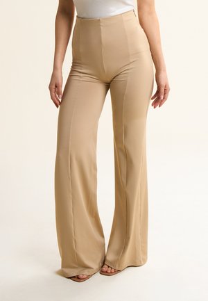 Pantaloni beige a vita alta realizzati in tessuto liscio con un design a gamba svasata e cuciture sottili, dotati di chiusura con zip laterale.