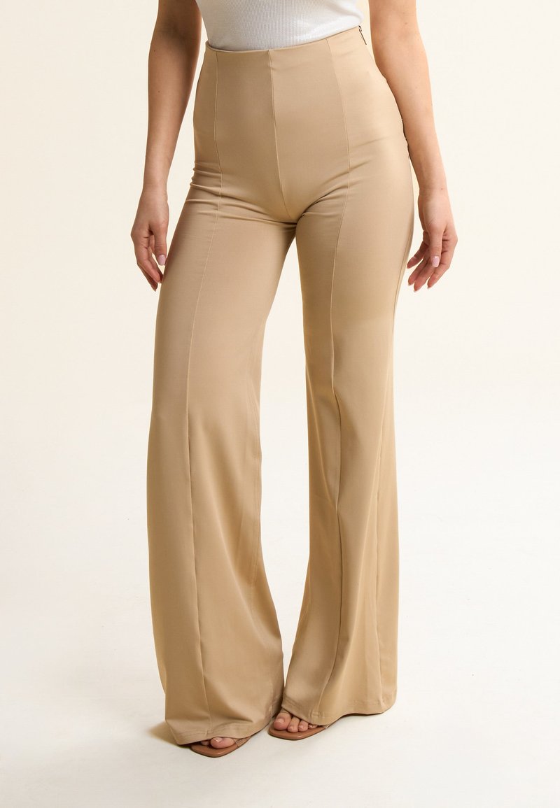 Pantaloni beige a vita alta realizzati in tessuto liscio con un design a gamba svasata e cuciture sottili, dotati di chiusura con zip laterale.