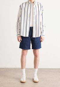 Lehká pruhovaná košile na knoflíky v bílé a modré barvě, v kombinaci s tmavými džínovými šortkami a bílými teniskami s béžovými podrážkami a ponožkami do crew délky.