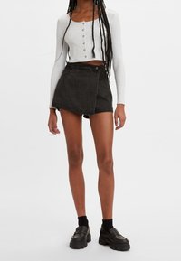 Vit ribbad långärmad crop-top med knappar, i kombination med en svart denimwrap-minikjol. Modellen bär klumpiga svarta loafers och strumpor.