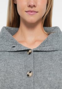 Pull en mélange de laine gris avec un col large, comportant trois grands boutons ronds et une finition douce et texturée.