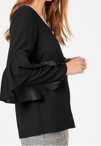 Black blouse with long ruffled sleeves and a V-neck. Made of smooth fabric, featuring an A-line design and a relaxed fit.