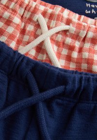 Deux paires de shorts en tissu texturé avec ceintures élastiques et cordons, un motif à carreaux rouge et blanc, l’autre en bleu marine uni.