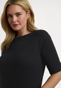 Μαύρο κοντομάνικο τοπ με στρογγυλή λαιμόκοψη, κατασκευασμένο από λείο ύφασμα. Διαθέτει χαλαρή εφαρμογή και λεπτές ραφές στους ώμους.