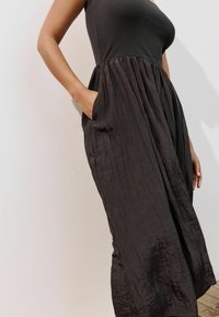 Robe noire avec un haut ajusté et une jupe plissée et fluide. Fabriquée en tissu léger, avec des poches latérales et une surface texturée.