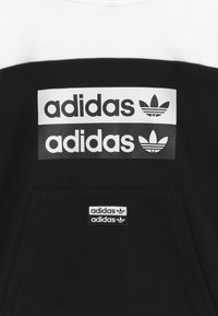 Sweat-shirt noir avec des accents blancs, présentant trois bandes horizontales avec le texte et le logo 'adidas', ainsi qu'une petite étiquette de marque sur la poche.