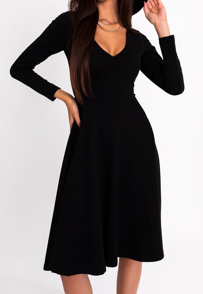 Robe noire à manches longues avec un corsage ajusté et une jupe évasée. Design en V, texture lisse et style minimaliste sans motifs supplémentaires.