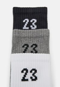 Tres pares de calcetines acanalados en negro, gris y blanco, cada uno con el número "23" tejido en colores contrastantes en el puño.