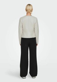 Jachetă din piele gri deschis cu un design structurat, ușor scurtă, combinată cu pantaloni largi negri, văzută din spate.