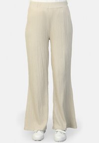 Helle beige, weit geschnittene Hose aus strukturiertem, geripptem Stoff mit einem elastischen Bund. Kombiniert mit weißen Schuhen für einen lässigen Look.